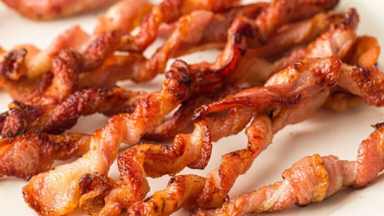 Close-up of several crispy, twisted strips of cooked bacon on a white surface.