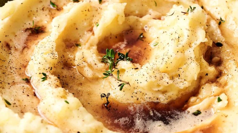 Creamy mashed potatoes topped with gravy and garnished with fresh thyme and cracked black pepper.