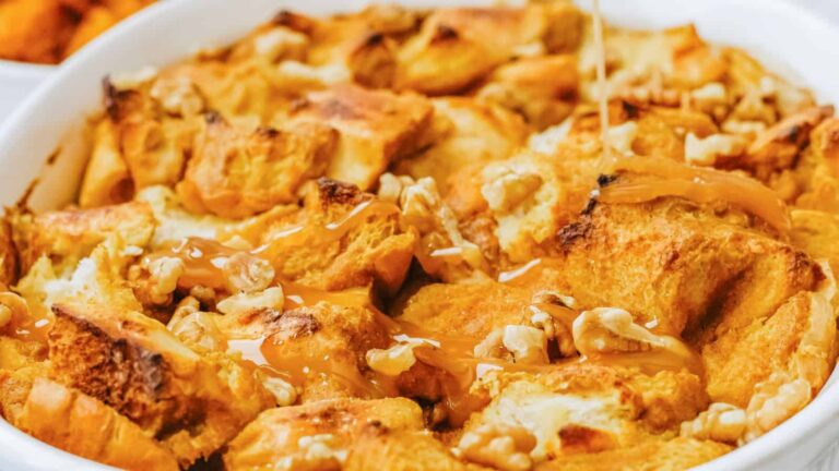 Close-up of a dish of bread pudding with walnuts drizzled with caramel sauce in a white baking dish.