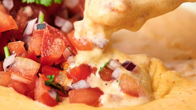 Cracker with creamy dip featuring bacon bits and green onions being lifted from a dish.