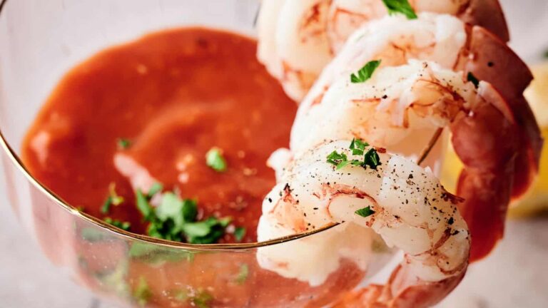 Shrimp cocktail with peeled shrimp arranged on the rim of a glass filled with cocktail sauce, garnished with parsley.