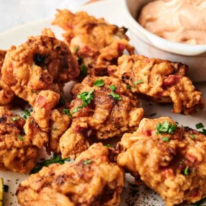 A plate of golden-brown fried chicken pieces and conch fritters garnished with herbs, served with a bowl of creamy dipping sauce.