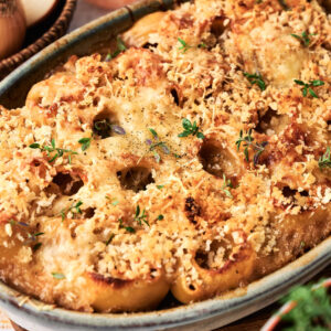 Baked pasta shells topped with golden breadcrumbs and melted cheese in a ceramic dish, inspired by French Onion Casserole, and garnished with fresh herbs.