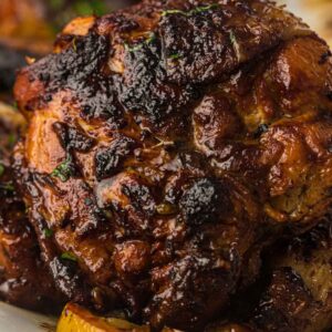 Close-up of a piece of roasted Miso Butter Chicken Thigh with a dark, caramelized crust, resting on slices of lemon on a white plate.