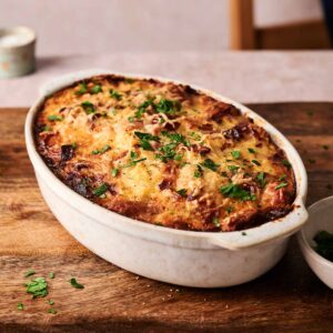 An Amish Breakfast Casserole topped with melted cheese and chopped parsley, served in a white oval dish on a wooden board.