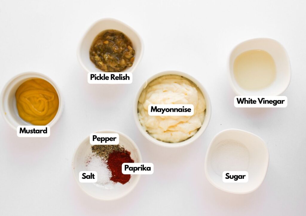 Six white bowls on a white surface contain labeled ingredients for Big Mac Pinwheels: mustard, pickle relish, mayonnaise, white vinegar, salt, pepper, paprika, and sugar.