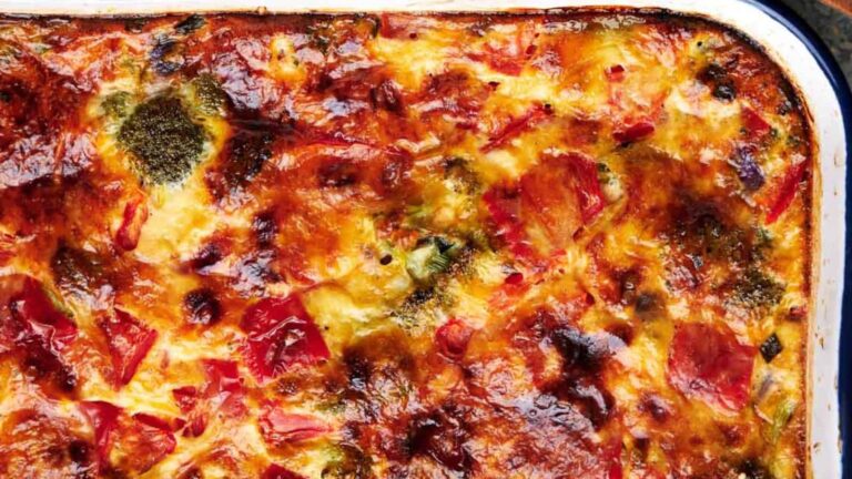 Close-up of a baked casserole with a golden-brown, slightly charred cheese topping and visible pieces of vegetables.