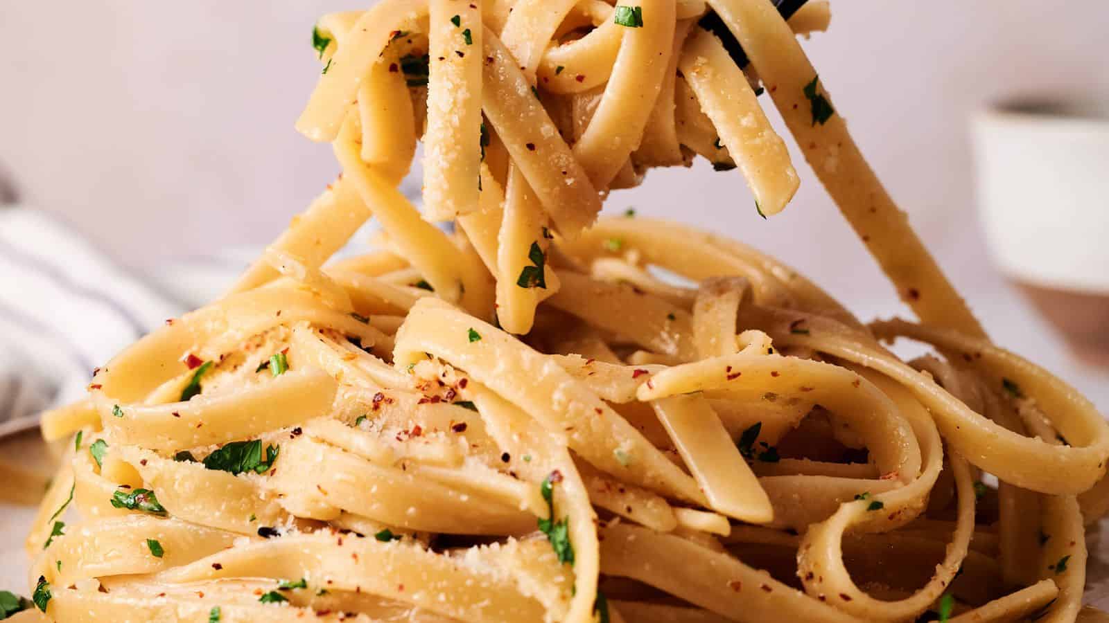 Close-up of fettuccine pasta tossed with grated cheese, chopped parsley, and red pepper flakes being lifted with a fork.
