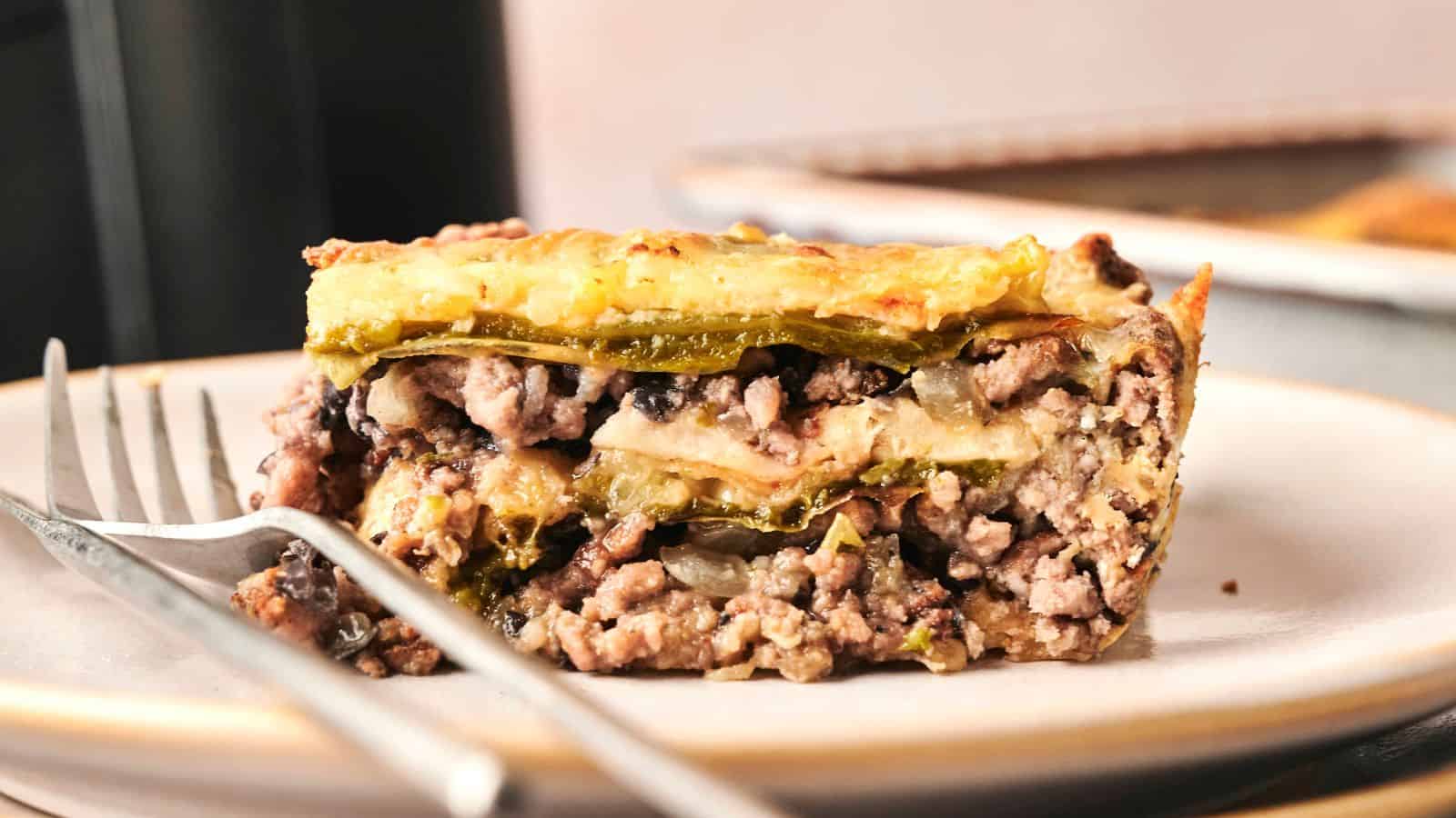 Close-up of a slice of layered casserole with ground meat, cheese, and vegetables on a plate with a fork.