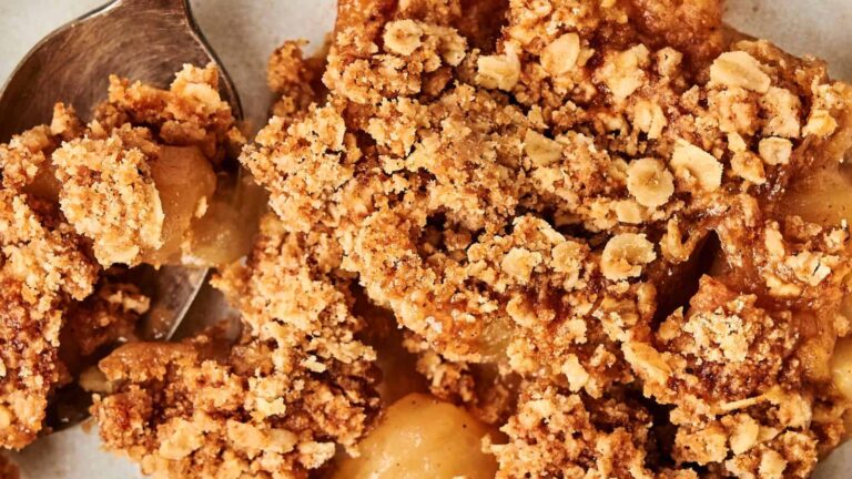 Close-up of apple crisp dessert with a crumbly oat topping, showing baked apple pieces and a spoon on the side.