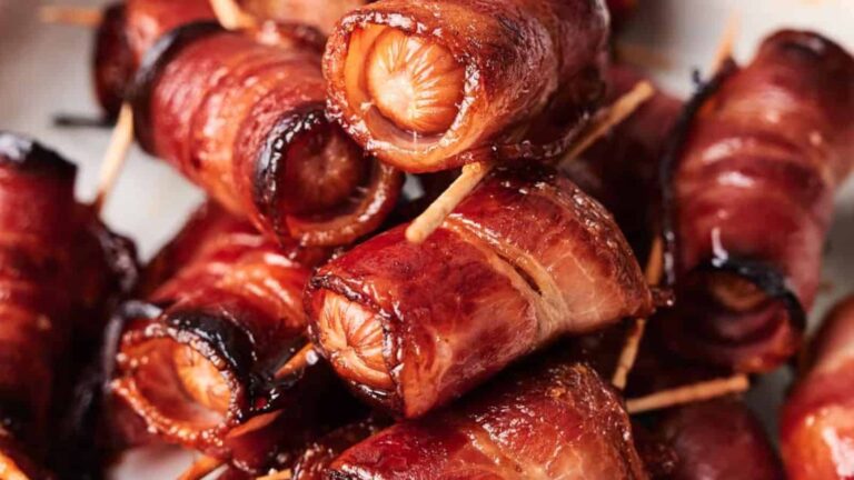 Close-up of bacon-wrapped sausages secured with toothpicks, stacked together and cooked to a golden brown.