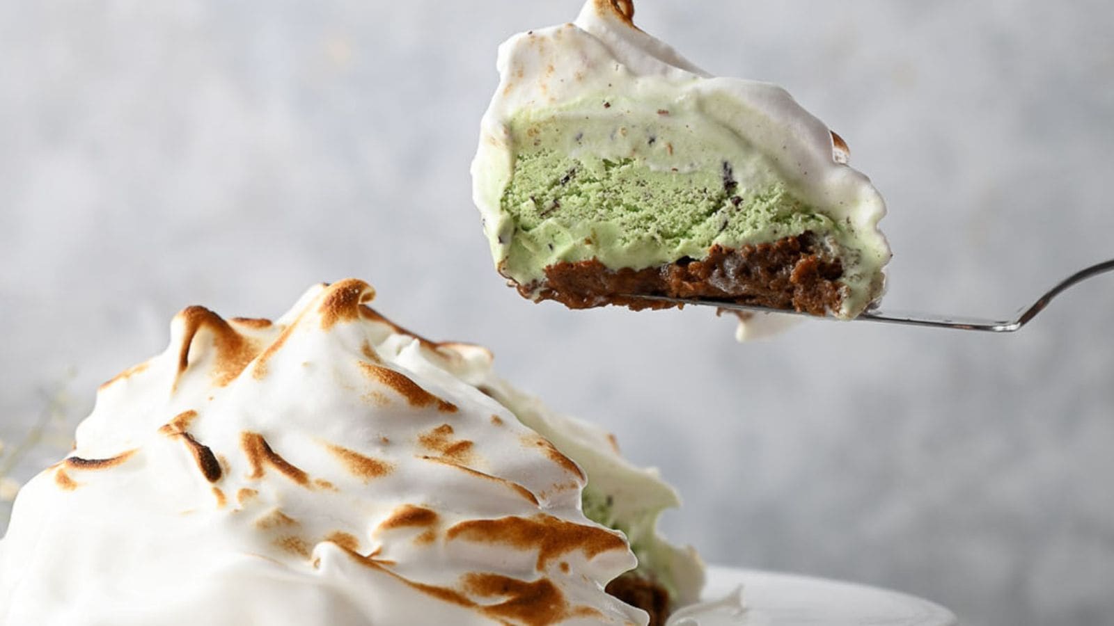 A slice of baked Alaska with a toasted meringue exterior and green ice cream center being lifted from the dessert.