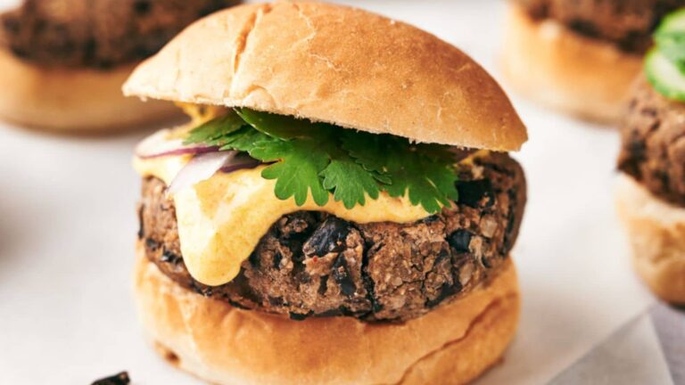A close-up of a black bean veggie burger topped with sauce, red onion, and cilantro, served in a sandwich bun.