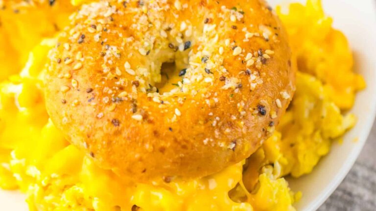 A close-up of a sesame-seed everything bagel sandwiching scrambled eggs with melted cheese.
