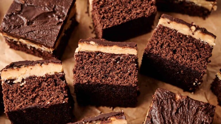 Several pieces of chocolate cake with a creamy filling layer and chocolate frosting on top, arranged on a sheet of brown parchment paper.