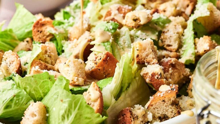 A close-up of a Caesar salad with romaine lettuce, croutons, grated cheese, and dressing.