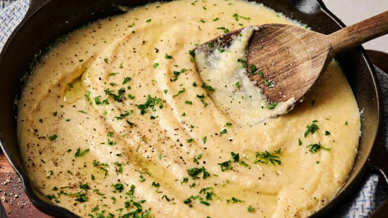 Creamy polenta in a cast iron skillet, garnished with chopped parsley and cracked black pepper, with a wooden spoon resting in the mixture.