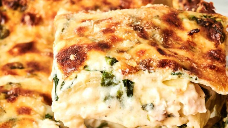 A close-up of a slice of creamy spinach and cheese lasagna with a browned, bubbly top layer.