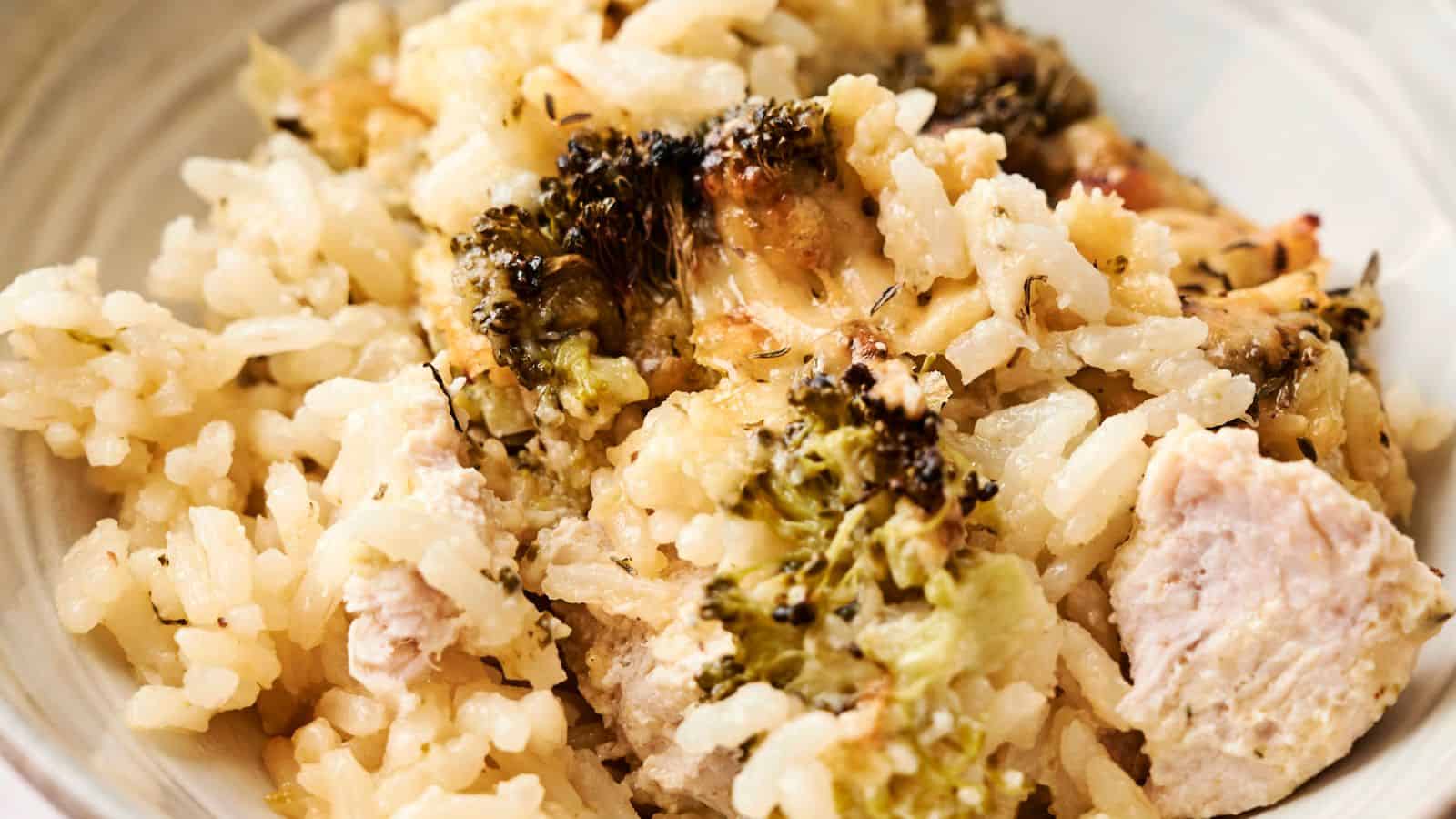 A close-up of a chicken and broccoli casserole featuring browned cheese, herbs, and green leafy garnish on top, displayed in a rectangular baking dish.