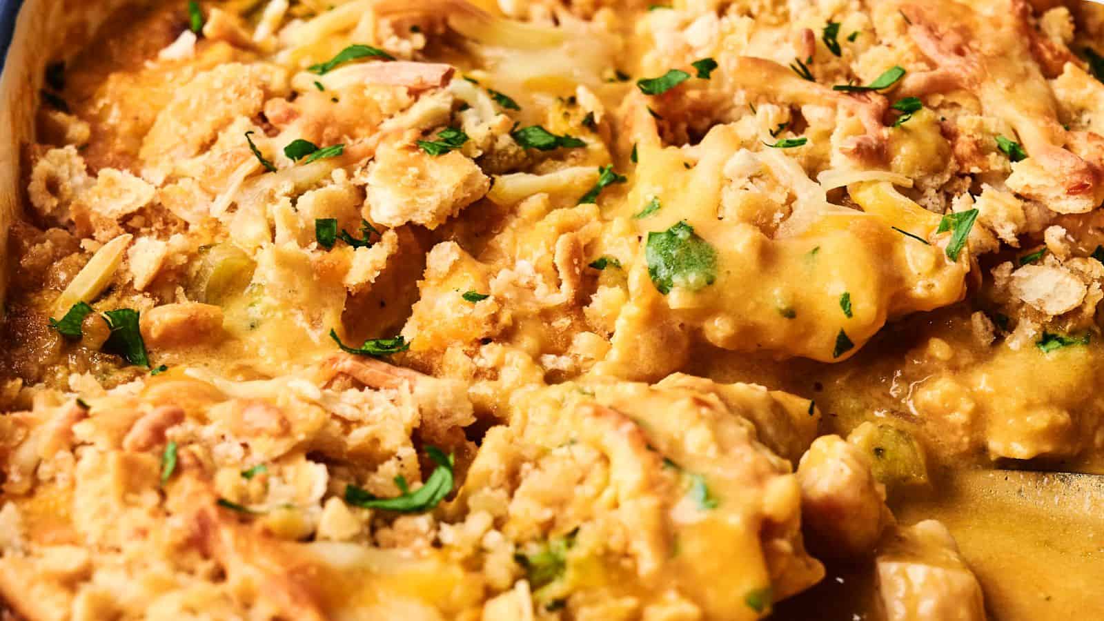 Close-up of a cheesy casserole topped with chopped parsley and crumbly bits, featuring melted cheese and a creamy texture.