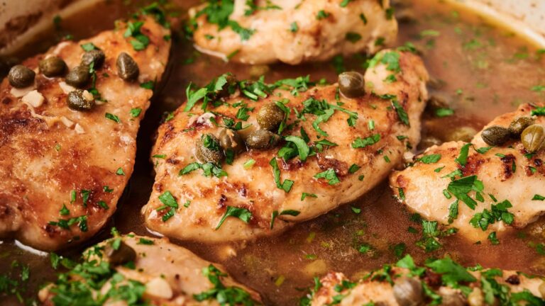 Chicken breasts cooked in a brown sauce, garnished with chopped parsley and capers.