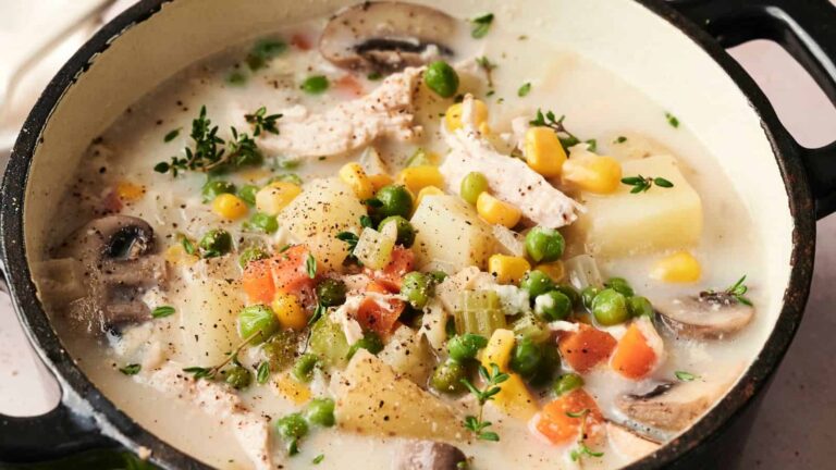A pot of creamy vegetable and chicken stew with peas, corn, carrots, potatoes, mushrooms, celery, and herbs simmering in broth.