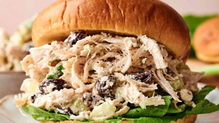 A shredded chicken salad sandwich with lettuce, raisins, and a creamy dressing served in a brioche bun.