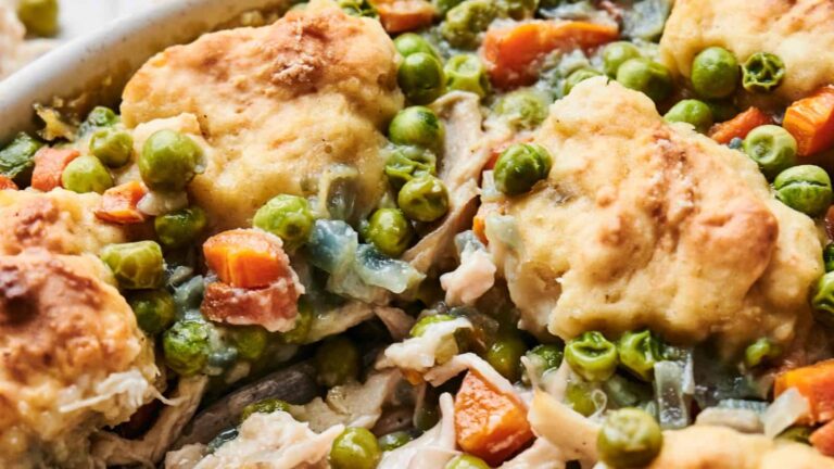 Close-up of a chicken and vegetable casserole topped with golden biscuits, featuring peas, carrots, and pieces of shredded chicken.