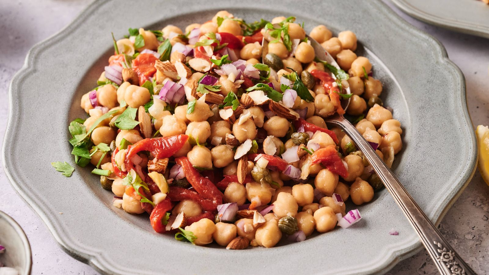 A plate of chickpea salad with chopped red onions, roasted red peppers, herbs, and sliced almonds, served with a spoon.