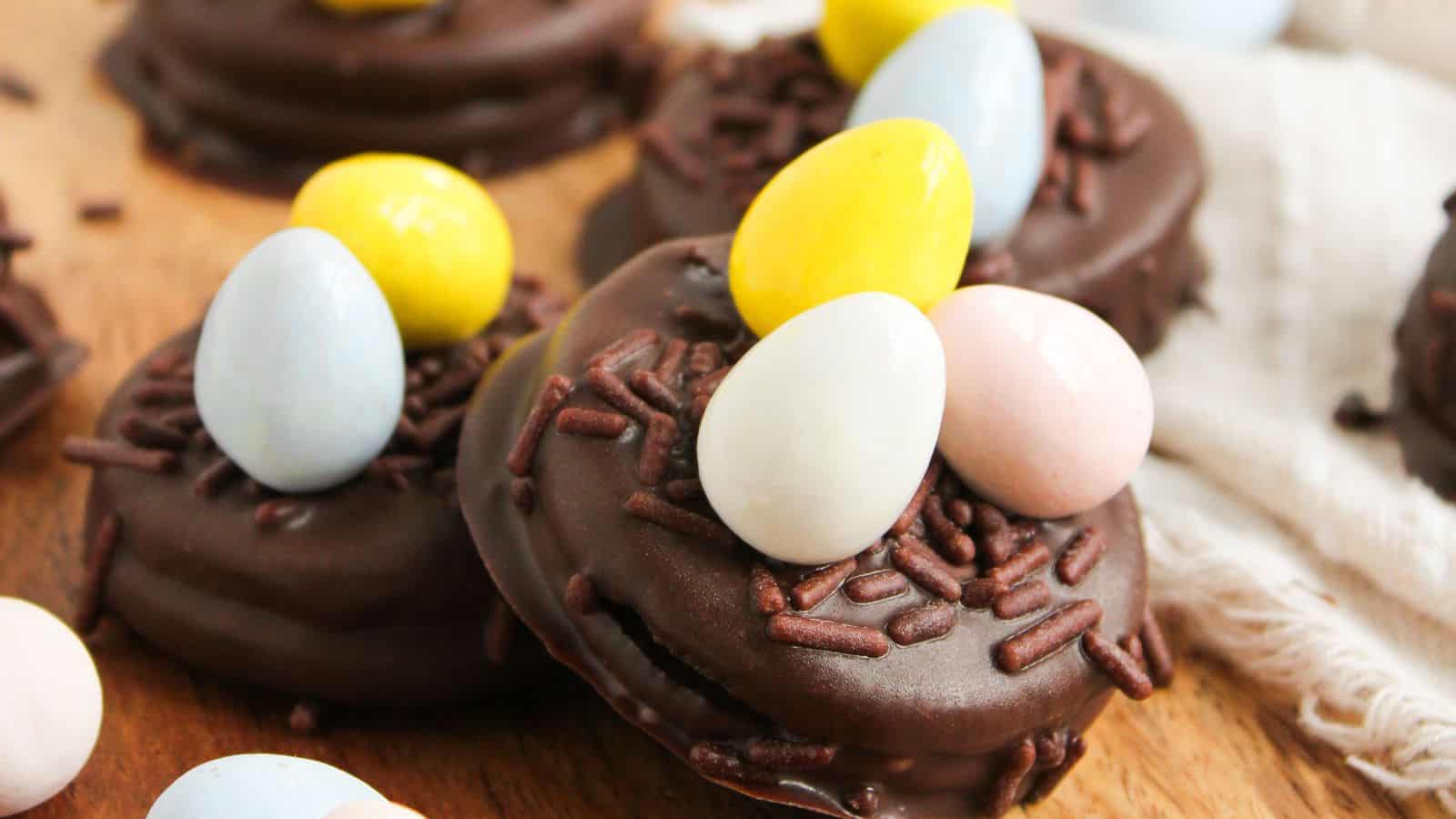 Chocolate cookies topped with colorful candy eggs and chocolate sprinkles on a wooden surface.