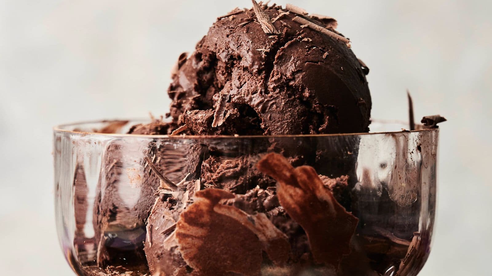 A glass bowl filled with scoops of dark chocolate ice cream topped with chocolate shavings.