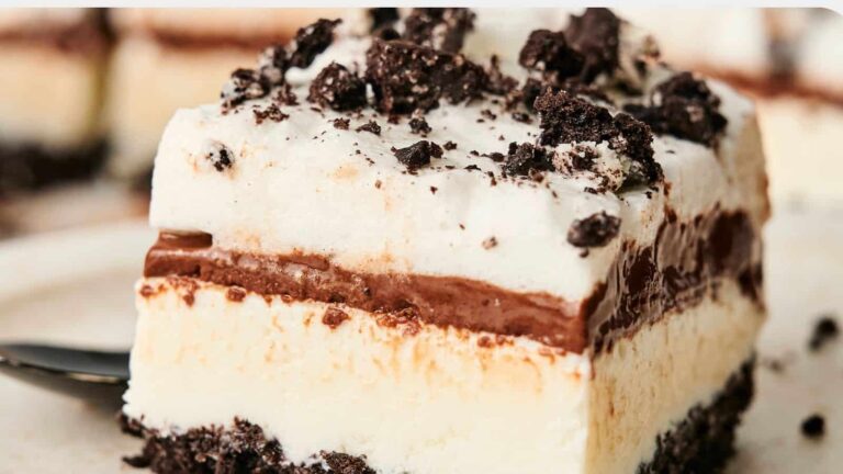 A close-up of a layered dessert with a crumbly chocolate base, creamy layers, chocolate filling, and crushed cookie topping.
