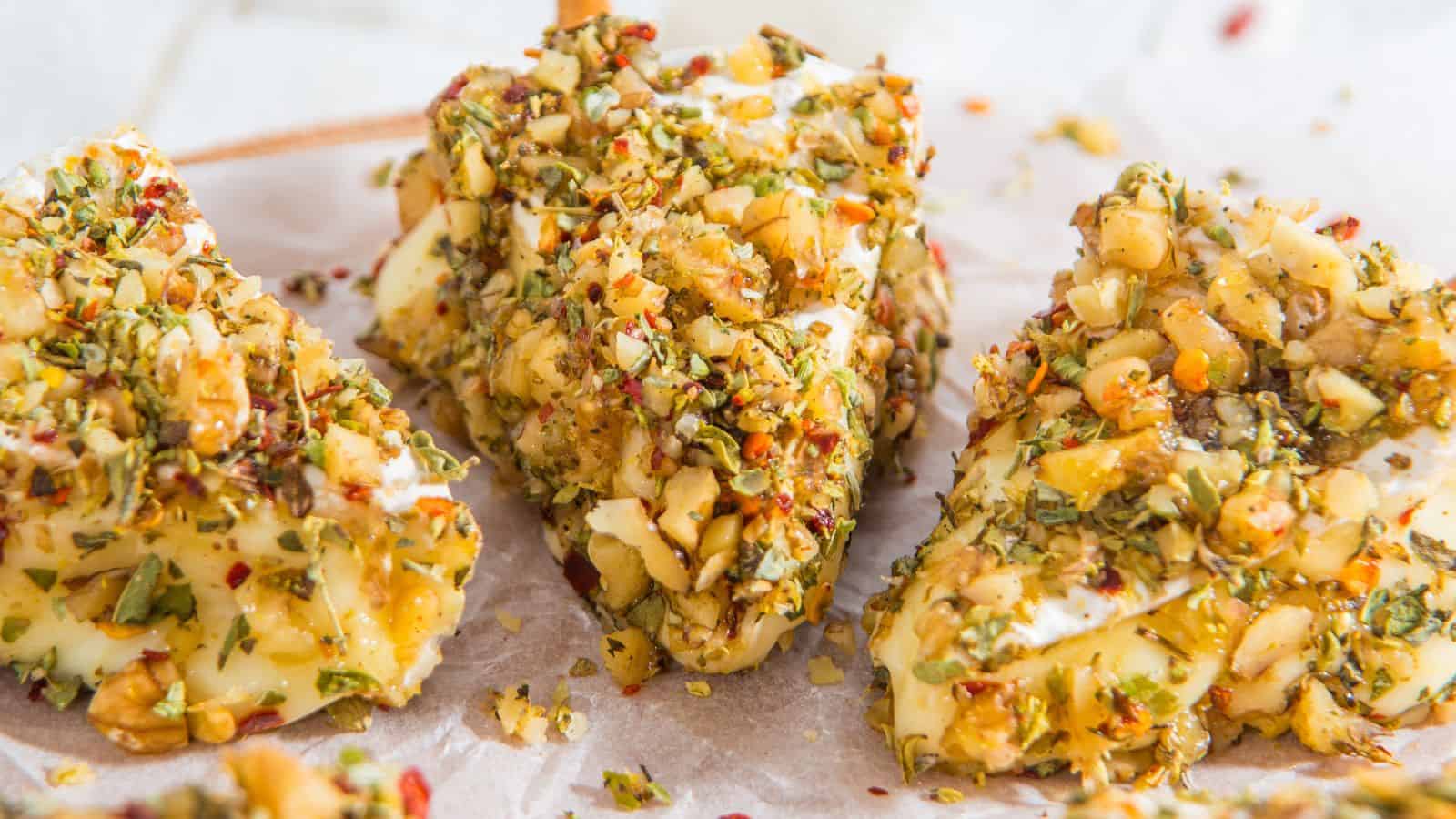 Close-up of sliced cheese coated with mixed herbs and chopped nuts on parchment paper, resembling charming Christmas cheese trees.
