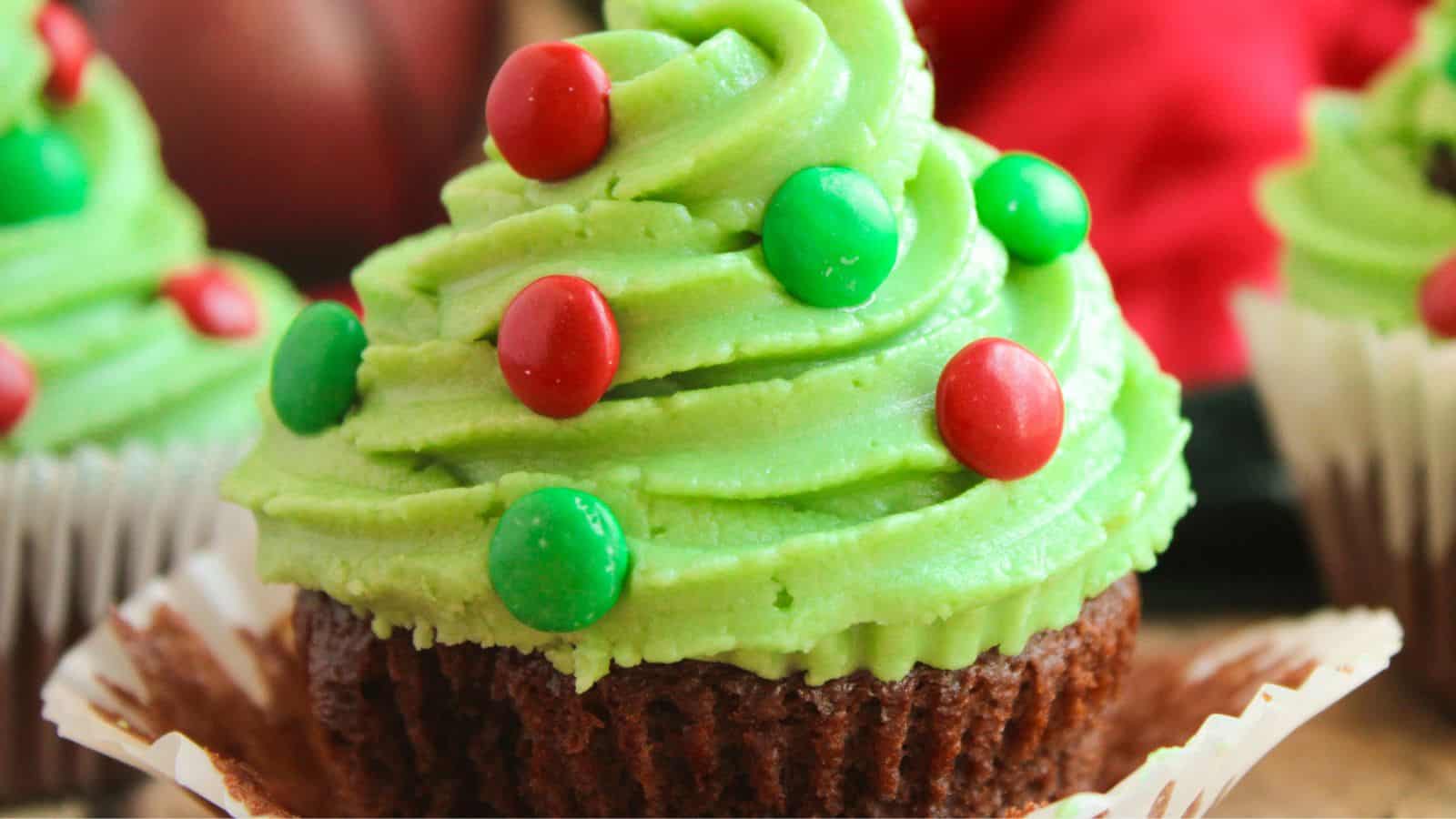 Cupcake with green frosting, adorned with red and green candy pieces, resembling a Christmas tree.