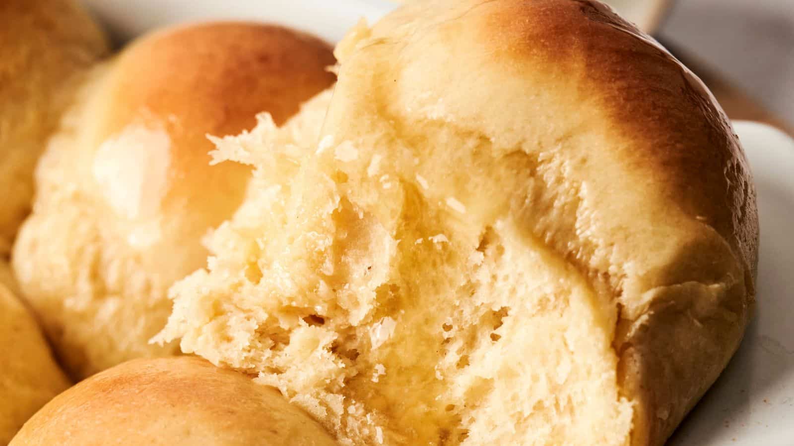Close-up of freshly baked golden-brown dinner rolls, with one roll partially torn to show its soft, fluffy interior.
