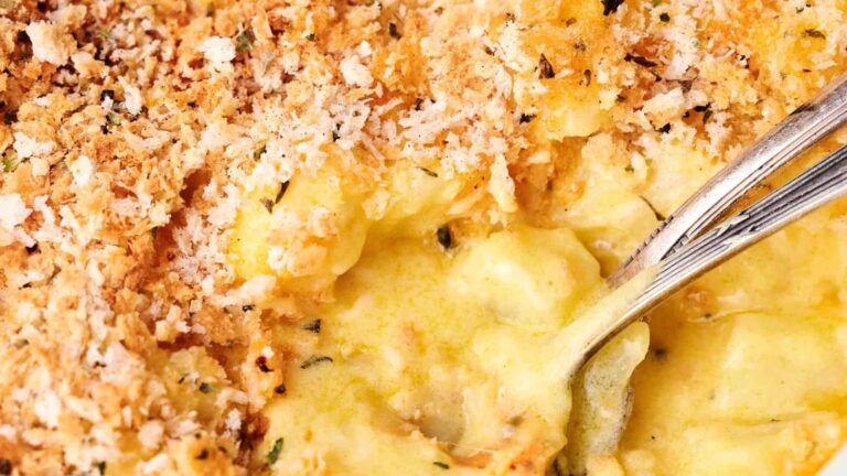 Close-up of a baked dish with a golden breadcrumb topping and a creamy, yellow filling being scooped with a spoon.