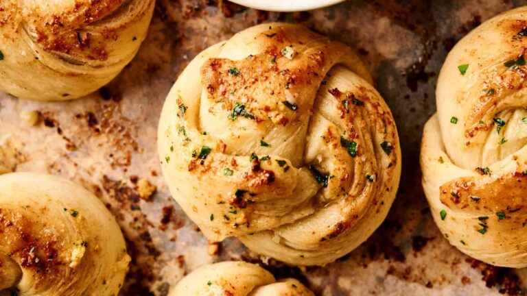 Close-up of freshly baked garlic knots topped with herbs and melted butter on a baking sheet.