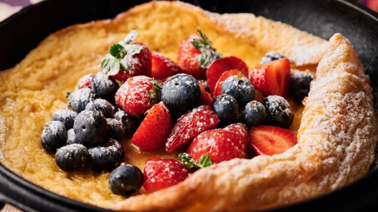 A Dutch baby pancake topped with fresh strawberries, blueberries, and a dusting of powdered sugar in a cast iron skillet.