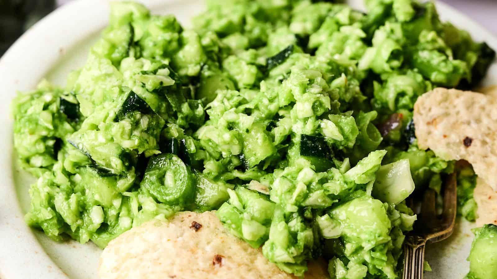 A close-up of a plate with bright green guacamole, chopped vegetables, and tortilla chips on the side.
