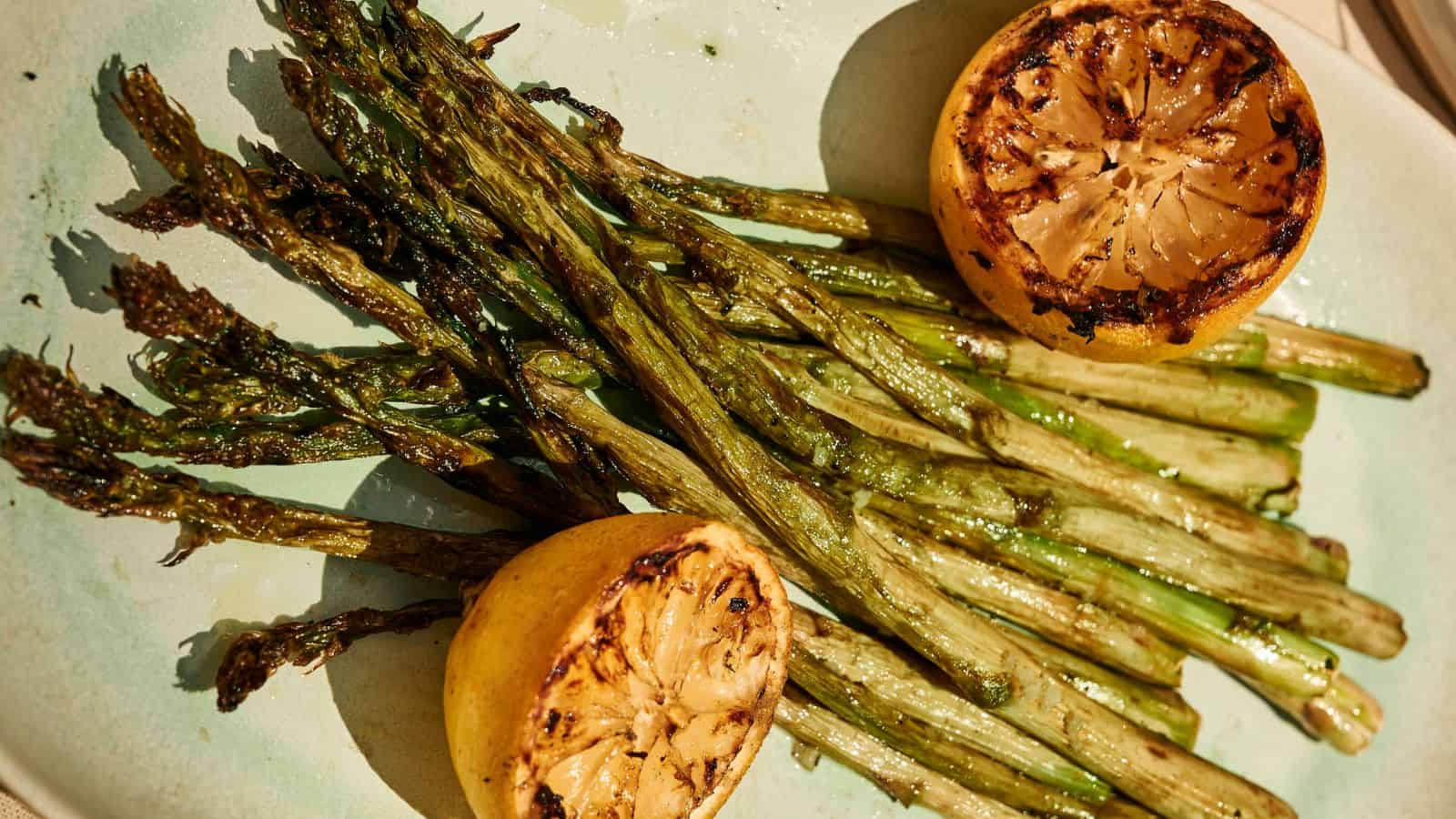 Grilled asparagus spears served on a plate with two charred lemon halves.