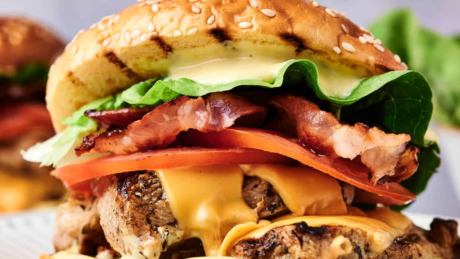 Close-up of a cheeseburger with a sesame bun, bacon, lettuce, tomato, cheese, and beef patty.