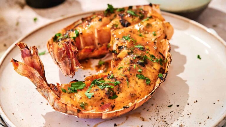 A cooked lobster tail served on a white plate, garnished with chopped herbs and sprinkled with pepper.