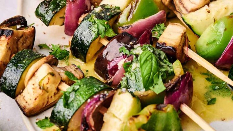 Grilled vegetable skewers with zucchini, eggplant, red onion, and green bell pepper garnished with fresh herbs.