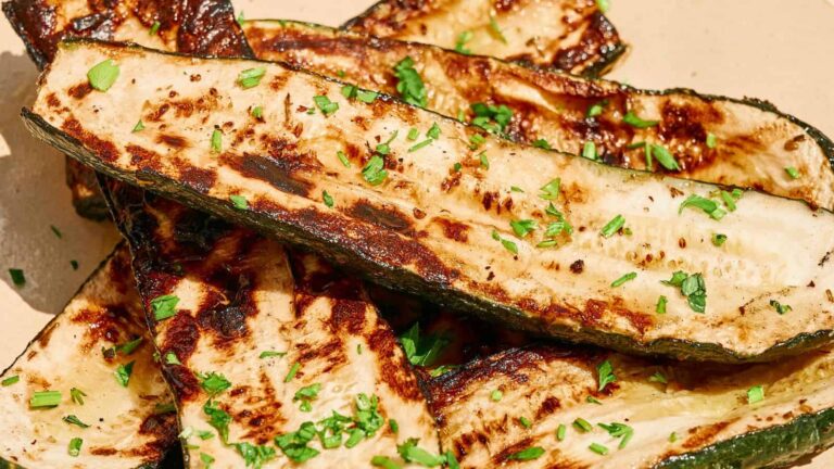 Grilled zucchini slices topped with chopped herbs on a beige plate.