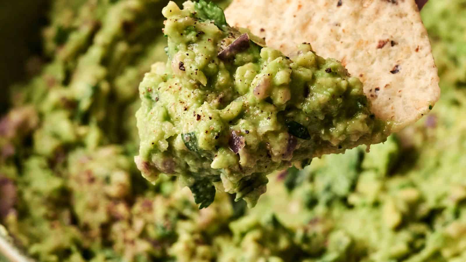Close-up of guacamole on a tortilla chip, showing a textured mixture of avocado, herbs, and spices.