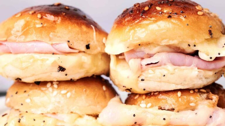 Four ham and cheese sliders with sesame seed buns, stacked in pairs, with melted cheese visible.