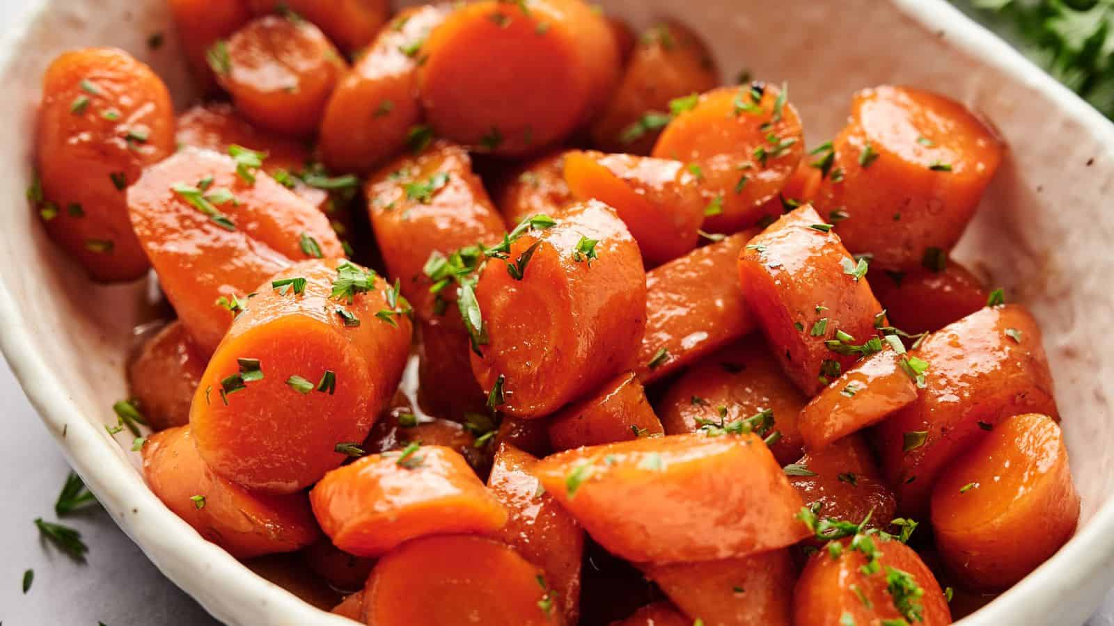 Close-up of a dish featuring glazed carrots garnished with chopped herbs, served in a white bowl.