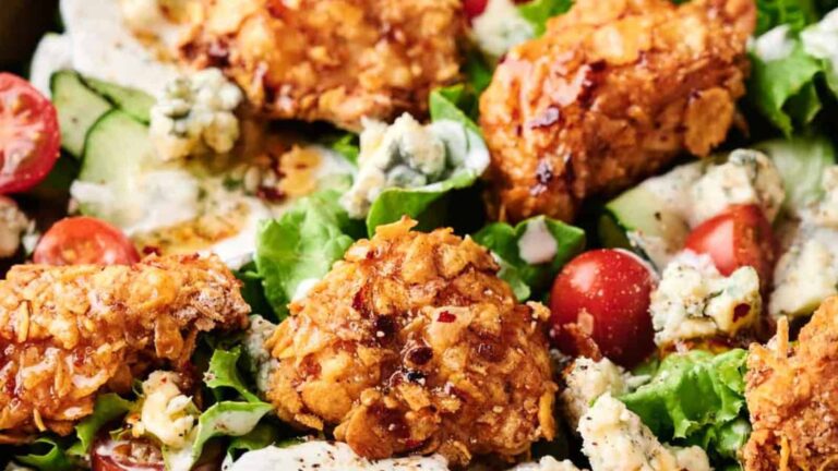 Crispy fried chicken pieces on a bed of lettuce with cherry tomatoes, cucumber slices, blue cheese crumbles, and creamy dressing.