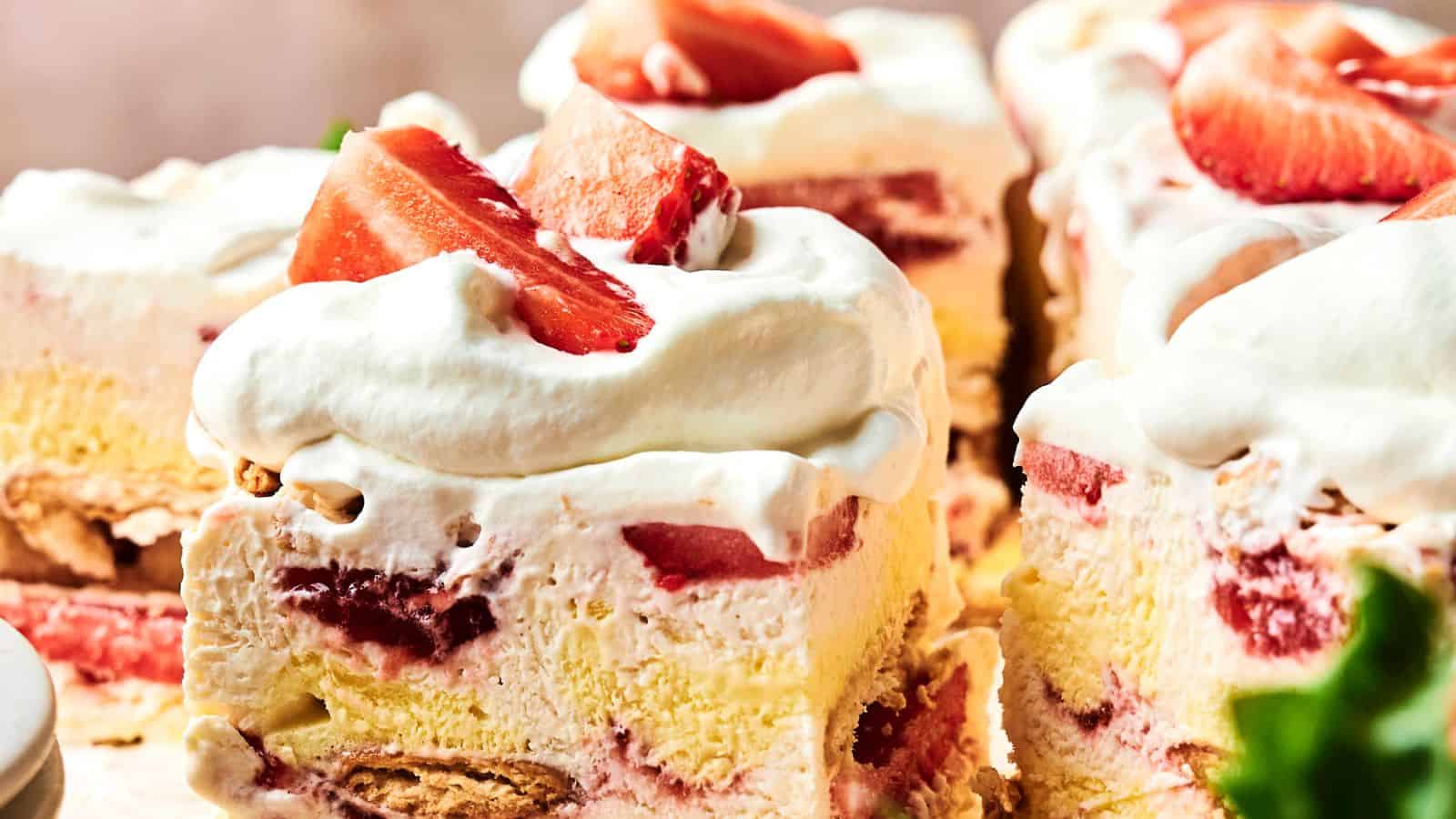 Close-up of strawberry shortcake slices topped with whipped cream and fresh strawberries. Layers of cake, cream, and strawberries are visible.