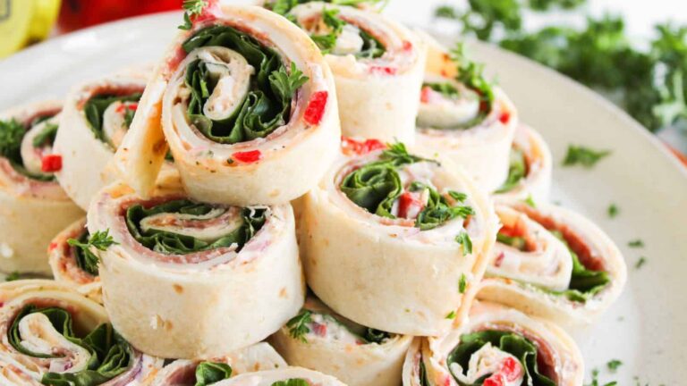 A plate of tortilla pinwheels filled with cream cheese, spinach, red bell pepper, and herbs, stacked in a pyramid shape.